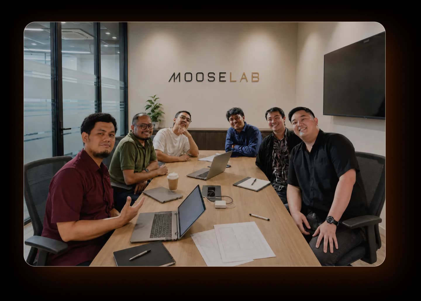 The Mooselab team gathered around the meeting room table beneath the Mooselab wall logo